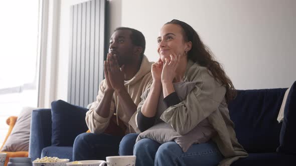 Excited Young Couple Relaxing At Home Sitting On Sofa Whilst Watching Sport On TV Together alt