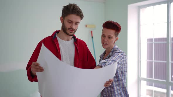 Slim Confident Caucasian Woman Talking with Man Examining Blueprint Pointing Away Leaving alt