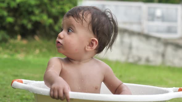 A Darkhaired and Cute Child Splashes His Hand in the Water Sitting in the Basin is Surprised By the
