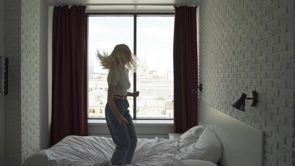 Young Funny Woman Cheerfully Jumps on the Big Bed in the Bedroom