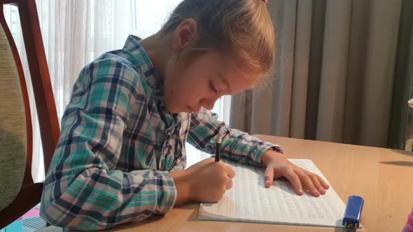 Child girl doing homework sitting at table, learning at home alt