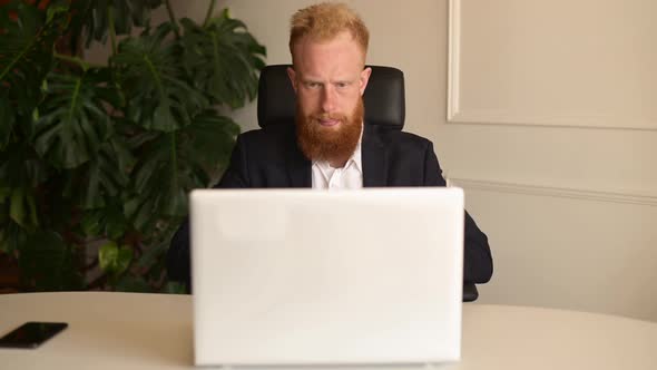 Focused Redhaired Businessman in Formal Suit Holding Video Call with Clients