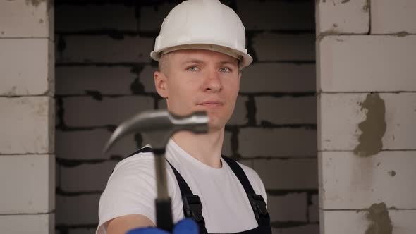 Portrait of a Construction Worker in a White Helmet with a Hammer in His Hands alt