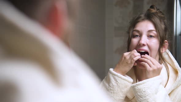 A Young Woman Puts a Corrective Aligner Splint on Her Lower Teeth to Correct an Overbite While alt