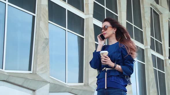 Portrait of a beautiful young woman holds a coffee and talk on the phone in the city center