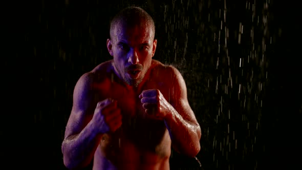 Slow Motion Shot of Fighter in Rain in Darkness Muscular Furious Man is Striking By Hands alt