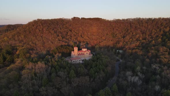 Aerial view of religious building nestled in the forest on a mountain with the sun shining in autumn