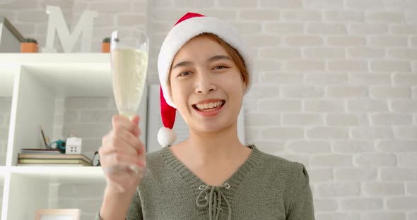 Woman wearing hat having video call celebrating Christmas online drinking and waving hand