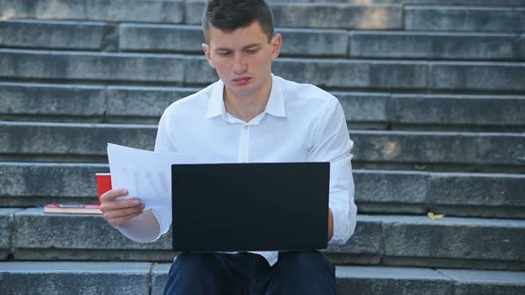 Trader Mat Sitting On Stairs And Looking On Financial Statements.