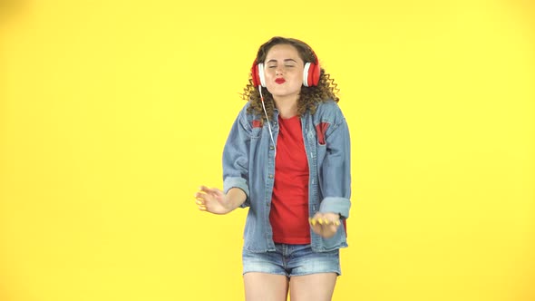 Cheerful Girl Dancing in Big Red Headphones on Yellow Background at Studio alt