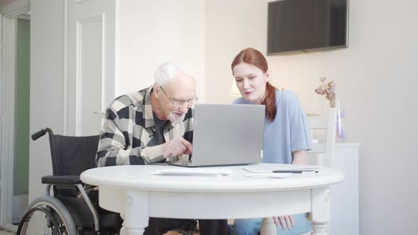 Woman Helping Disabled Grandfather Understand How to Use Laptop alt