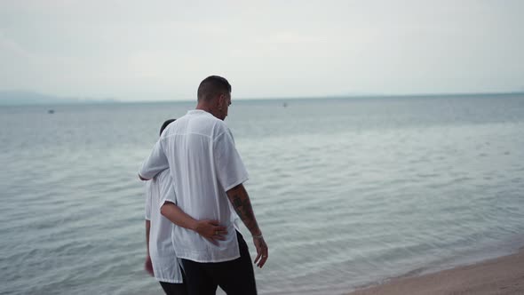 Married Gay Couple Men Walk By the Sea on a Beach During Honeymoon Trip  Back View alt