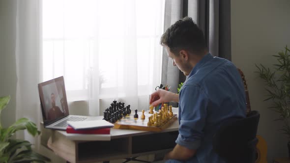 A Young Cute Man Plays Chess with a Different Video of a House During a Pandemic alt