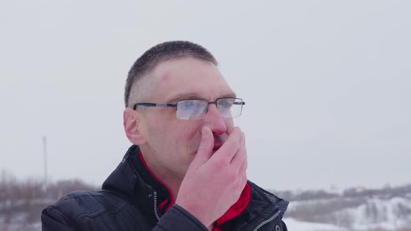 Man He Runs His Hand Over His Nose and Sniffles Standing Outside in Cold Weather in Winter alt