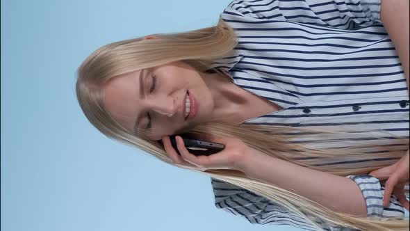 Pleasant-looking Young Lady Speaking with Somebody By Smartphone on Blue Background. alt