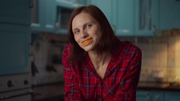 Young smiling 30s woman playing with orange peels in her mouth alt