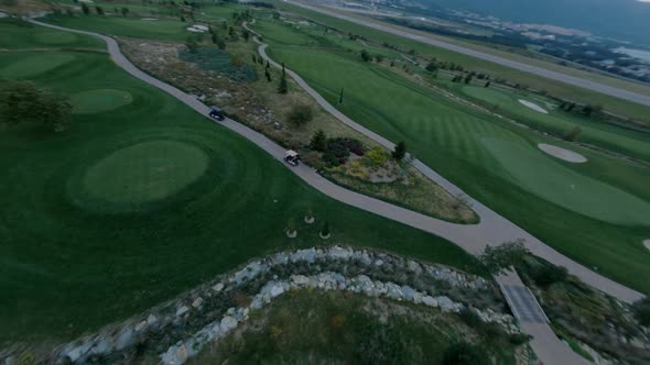 FPV Drone Evening Golf Cars Riding on Path Field Covered By Green Natural Lawn alt