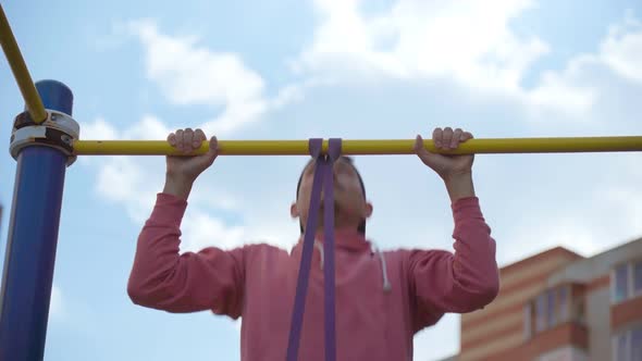 A Young Man Performs Pullup Exercises with Fitness Elastic Bands on the Street alt