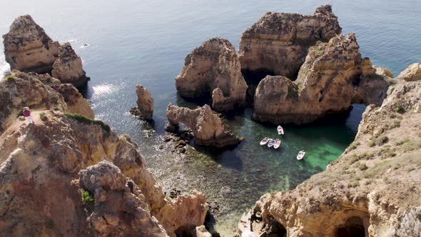 Visitors taking photos on top of cliff, Lagos , Algarve. Boats moored on shallow sea water alt