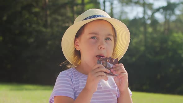 Cheerful Preschool Girl in a Straw Hat Eating a Sweet Chocolate Park Summer alt