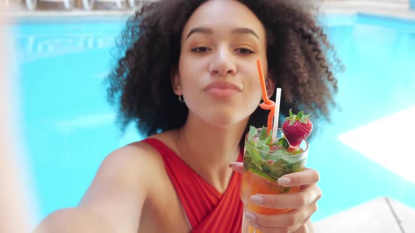 Young Girl Teenager Internet Vlogger Poses in Front of Camera with Cocktail in Pool, Folds Bow Her alt