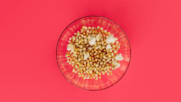 Corn seeds popping up from glass bowl. Popcorn preparation.Delicious salty snack alt