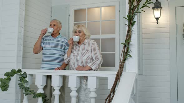Senior Elderly Caucasian Couple Drinking Coffee, Embracing in Porch at Home. Mature Happy Family alt