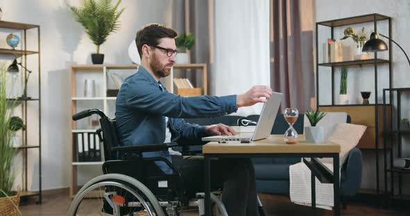 Handicapped Man in Wheelchair Working on Laptop in Home Office at daytime alt
