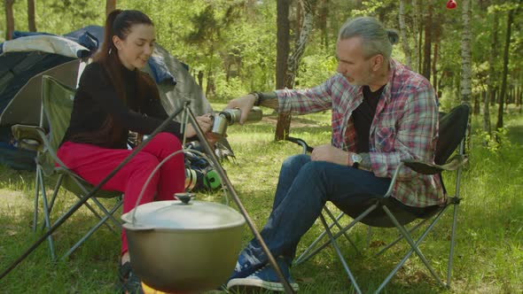 Relaxed Backpackers Pouring Hot Drink Into Travel Mug From Thermos at Campsite alt