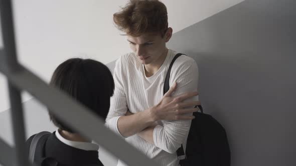 Closeup of Shy High School Student Standing at Wall on Stairs As Confident Girl Kissing Boy on Cheek alt