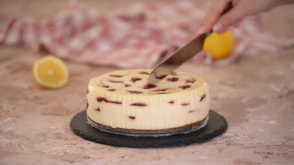 Pastry chef cuts cherry cheesecake.	