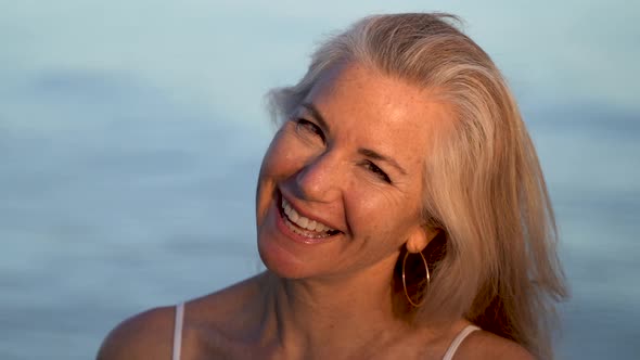 Blonde mature woman laughing and smiling looking and flirting with the camera in a portrait. alt