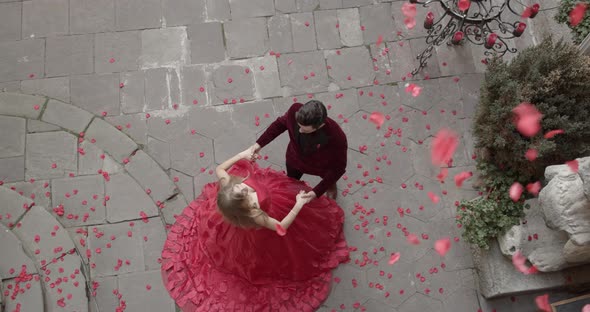 Girl And Guy Stand In Festive Attire And Rose Petals Fly From Above alt