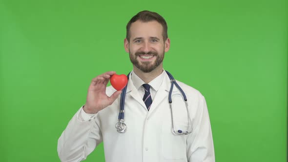 Young Male Doctor Holding a Heart Shape and Smiling Against Chroma Key alt