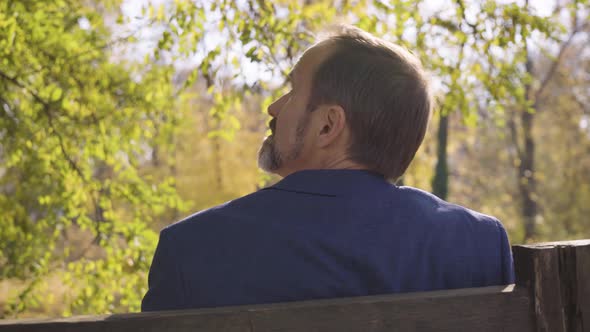 A Middleaged Handsome Caucasian Man Looks Around As He Sits on a Bench in a Quaint Town in Fall