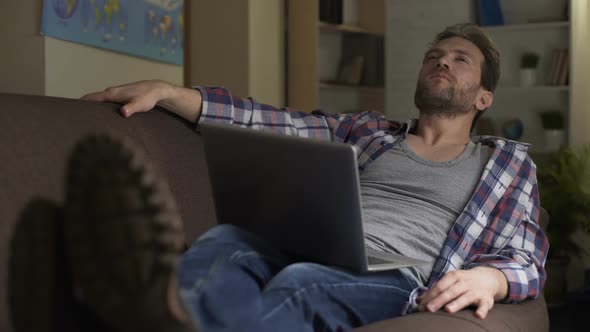 Adult Man Sitting on Sofa With Computer on Lap Thinking, Future Plans, Choice alt