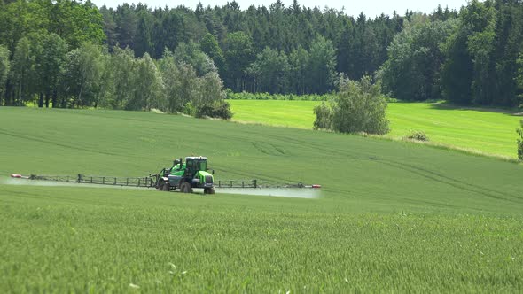 A View of Green Fields with Trees and Bushes, Tractor Drives on the Filed and Sprays the Grass. alt