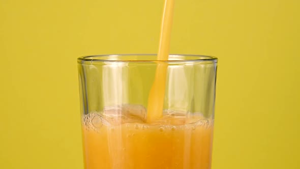 Pouring orange juice in glass over yellow alt