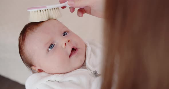 Mom Gently Combs The Hair Of Her Newborn Baby
