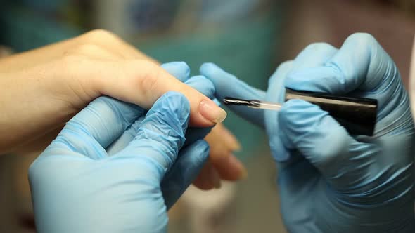 Manicurist in Blue Gloves Paints Nails. Applies Gel Polish To the Nail Plate