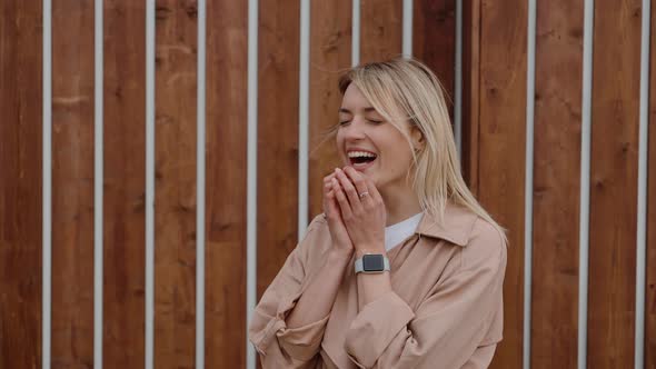 Pretty Blonde Girl Is Laughing on Street Waving By Hands Around Her Face alt