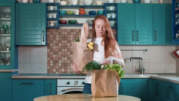 Young woman unpacks groceries from paper bag in modern kitchen home alt