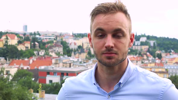 Young Handsome Business Man Looks To Camera with Serious Face - City in Background - Closeup alt