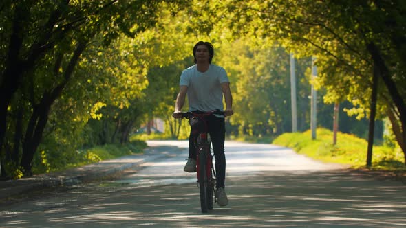 Young Smiling Happy Man in White Shirt Riding a Bike with His Hands Apart alt