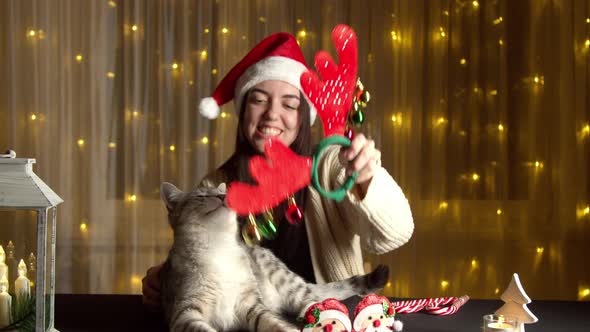 Stylish Happy Girl in Santa Hat Playing with Cute Cat