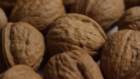 Cinematic, rotating shot of walnuts in their shells on a white surface alt