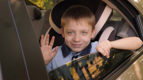 A Boy is Wearing a Seat Belt in a Child Seat in the Car He Waves His Hand alt