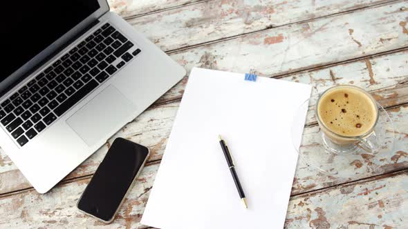 Coffee cup, laptop, mobile phone, clipboard, pen on wooden plank alt