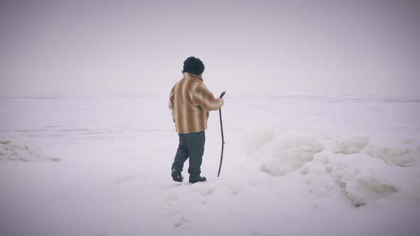 Wide Shot Winter Landscape with Indigenous Senior Man Walking with Stick in Slow Motion alt