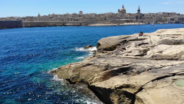 Aerial view towards Valletta, Malta with waves splashing rocky limestone Sliema beach in sunny summe alt